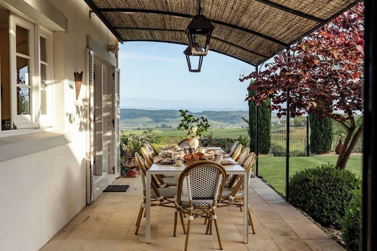 Eine überdachte Terrasse mit Esstisch, mit Blick auf eine reizvolle Landschaft.