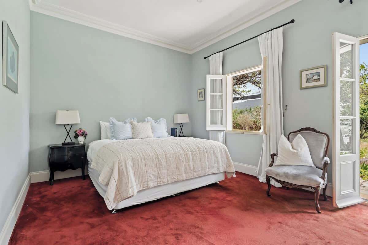 A bedroom with a large bed, a nightstand, a chair, and a window with curtains.