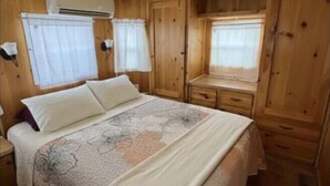A cozy cabin-style bedroom with a large bed, wooden walls, and a small window. - Little Lantern Cabin (Indianapolis)