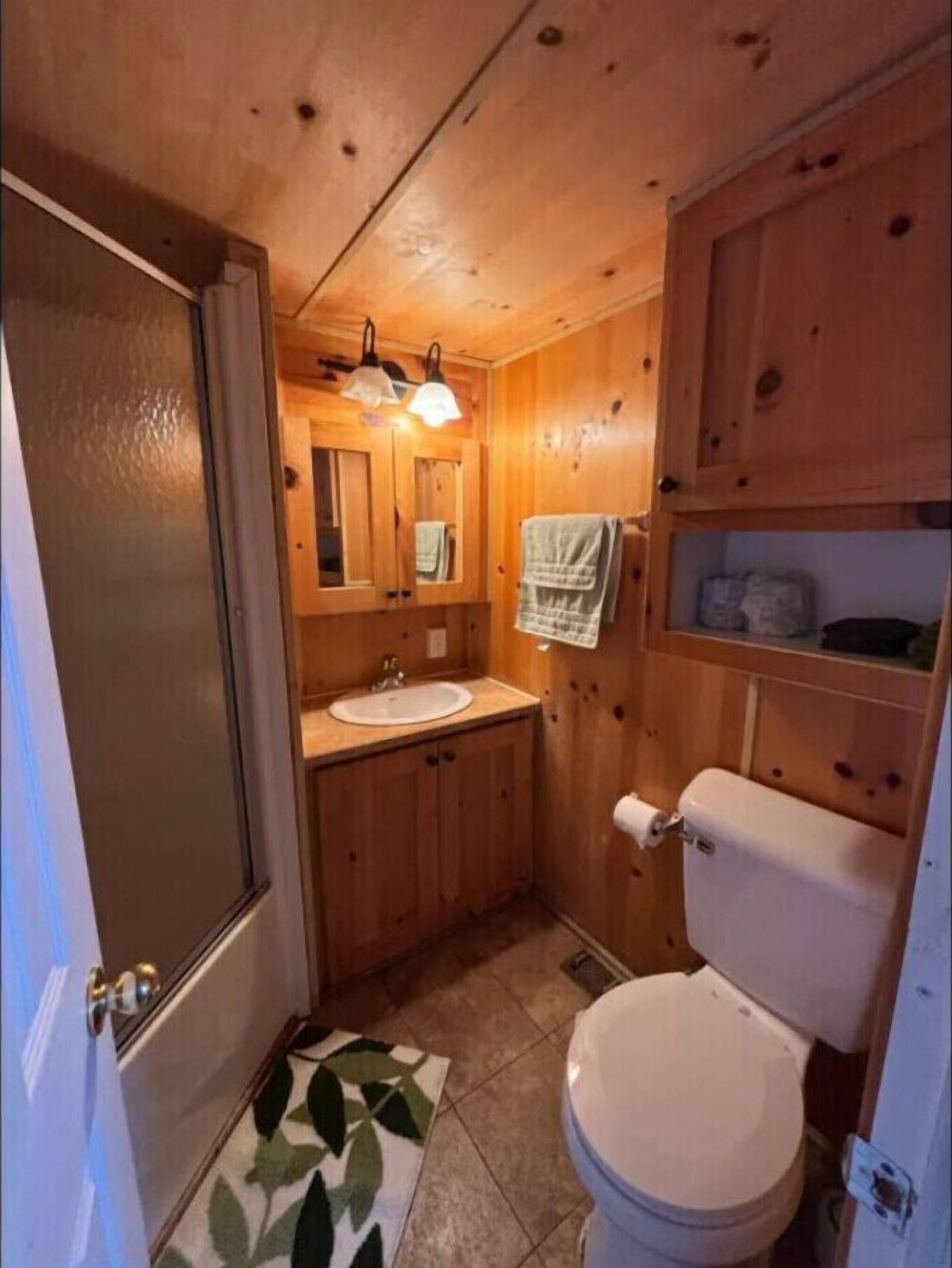 A compact wooden bathroom with a sink, toilet, and a mirror above it.
