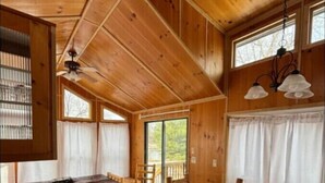 A wooden cabin interior with a dining table, chairs, a bench, and a ceiling fan.