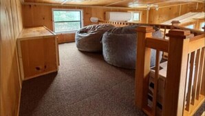 A cozy cabin interior with a wooden ceiling, a window, a bed, and a small table.