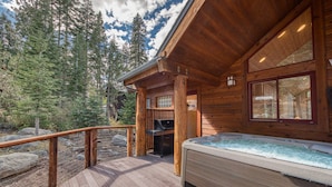 Une cabane en bois dotée d’un bain à remous, d’une terrasse et offrant une vue sur la forêt environnante.