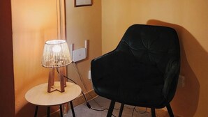 Ein Zimmer mit einem schwarzen Sessel, einem runden Tisch mit Lampe und drei gerahmten Kunstwerken an der Wand.