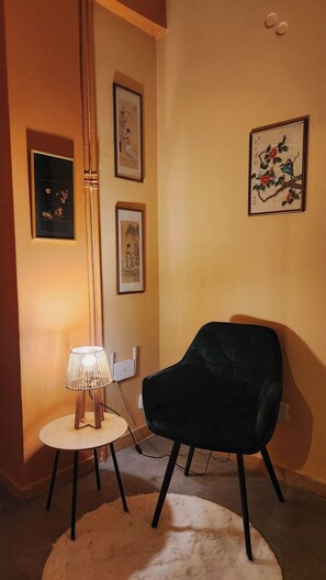 Una habitación con un sillón negro, una mesa redonda con una lámpara y tres obras de arte enmarcadas en la pared.