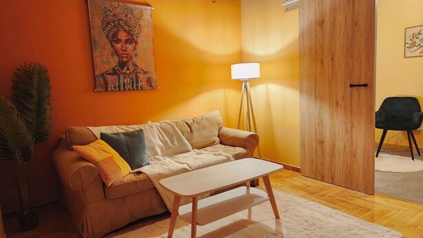 Ein Wohnzimmer mit einem beigen Sofa, einem weißen Couchtisch, einer Stehlampe und einem Bild an der Wand.