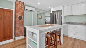 Una cocina moderna con armarios blancos, una pared de ladrillo decorativa, un refrigerador de acero inoxidable y una isla de madera con taburetes.