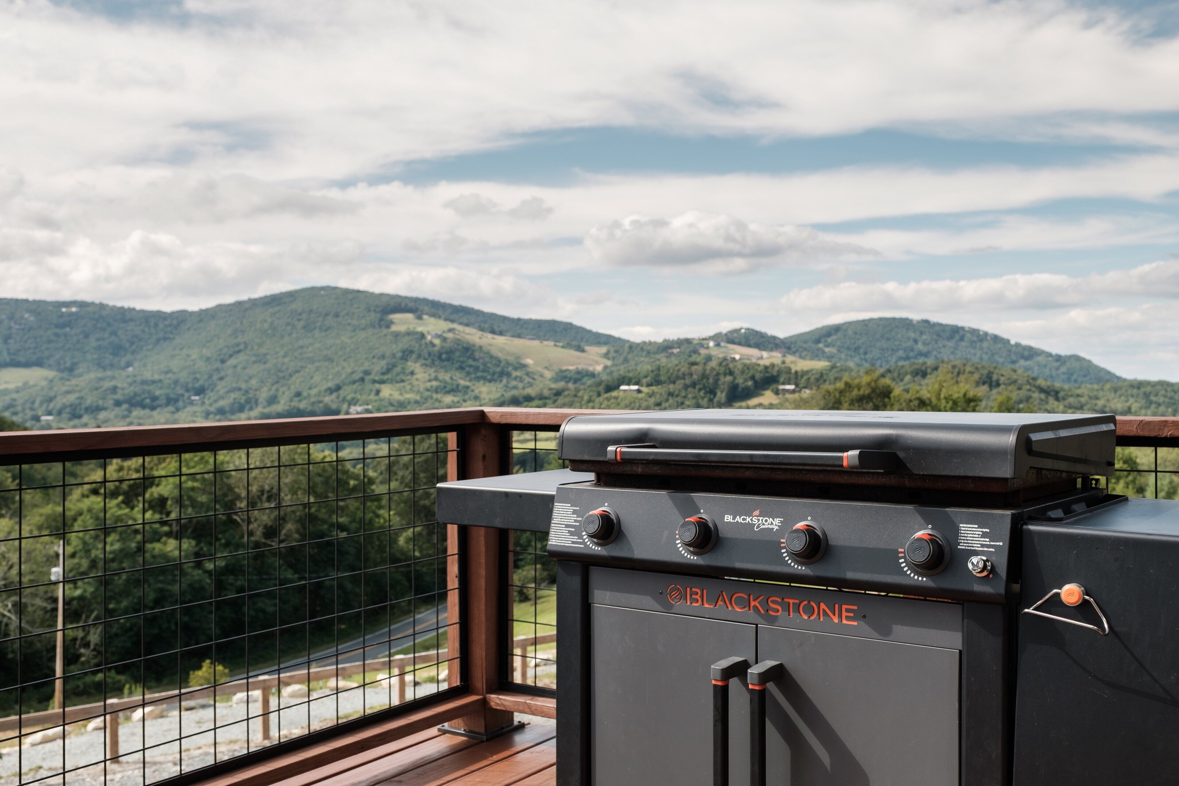 Een Blackstone grill op een balkon met uitzicht op groene heuvels en een bewolkte lucht.