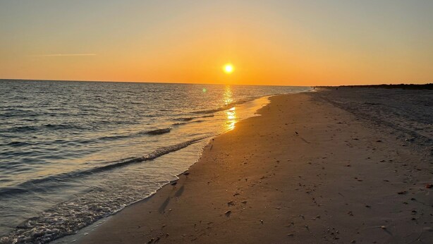 Una playa al atardecer, con aguas tranquilas y cielo despejado.