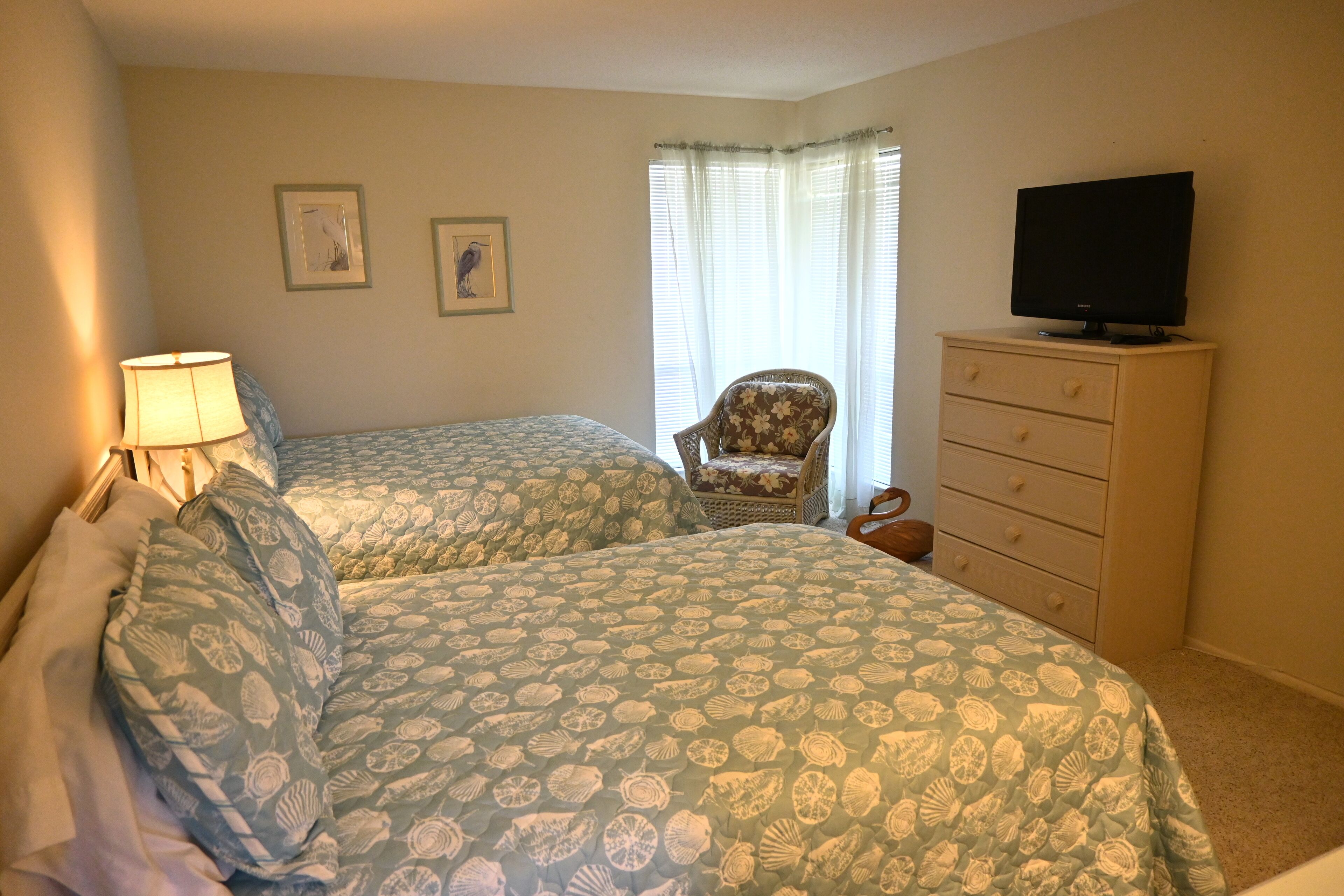 Une chambre avec deux lits, une chaise, une commode et un téléviseur.