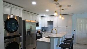 Cocina moderna con electrodomésticos de acero inoxidable, armarios blancos y una isla central con taburetes de bar.