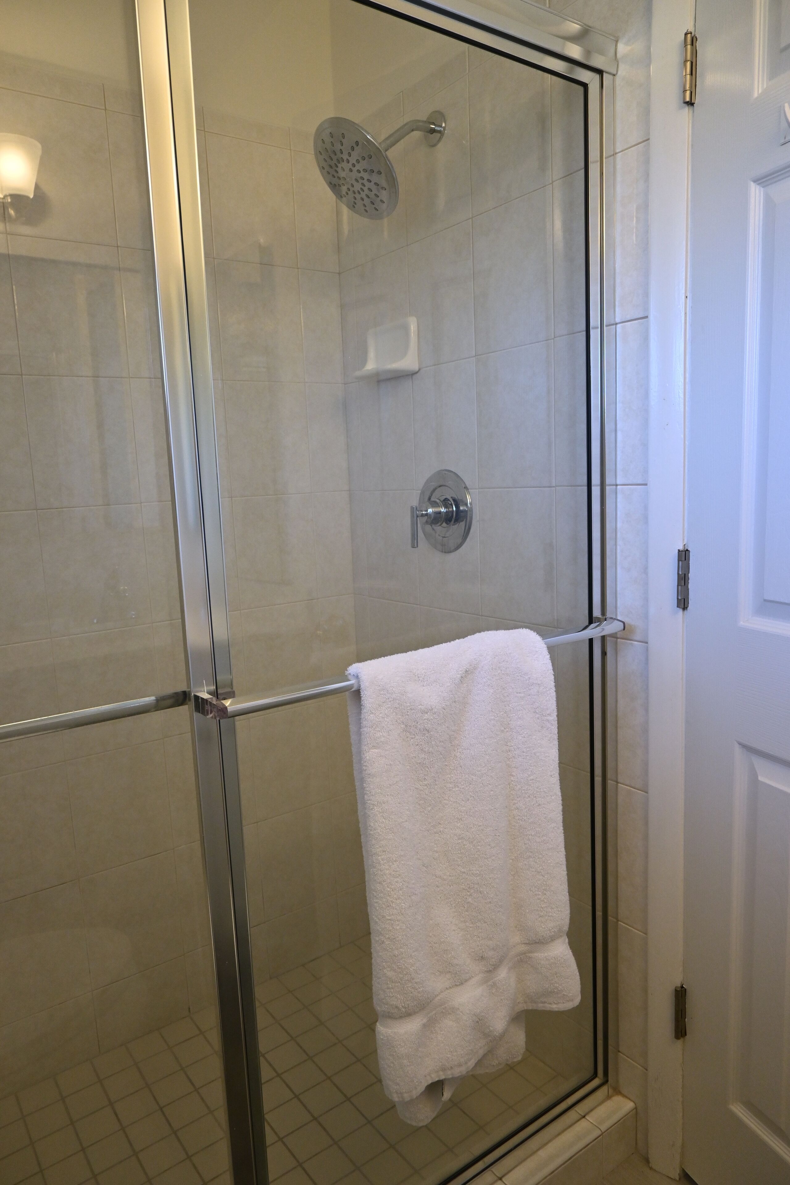 Une douche fermée par des parois de verre, avec une serviette blanche suspendue à une barre métallique.