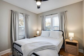 Quarto com cama, duas mesas de cabeceira com abajures e uma janela com cortinas.