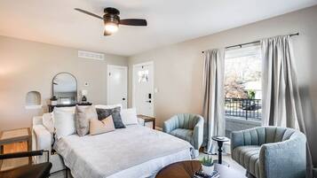 Une chambre d’hôtel comprenant un lit, deux fauteuils, un bureau, un ventilateur de plafond et une fenêtre avec des rideaux.