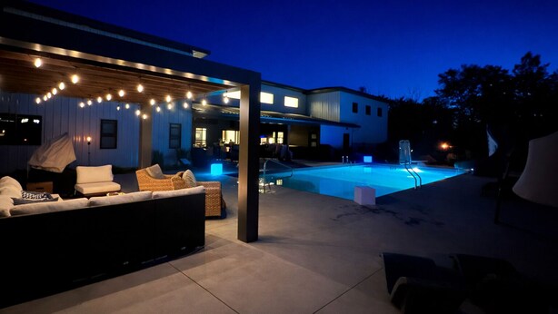 A modern outdoor pool area with a covered seating area and string lights. - Pure MUCHigan (Holland)