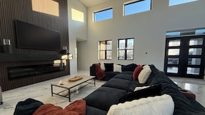 A modern living room with a sectional sofa, a flat-screen TV, a fireplace, and large windows. - Pure MUCHigan (Holland)