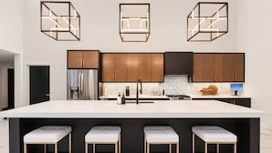 A modern kitchen with a large island, bar stools, and pendant lighting. - Pure MUCHigan (Holland)