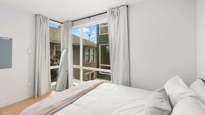 A bedroom with a large bed, white curtains, and a view of a house through a sliding glass door. - 2026 World Cup | Rooftop View, Light Rail, Parking (Seattle)