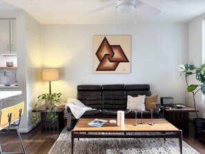 A modern living room with a black leather sofa, a wooden coffee table, a floor lamp, and a painting on the wall. - the escape: king bedroom w/pool, hot tub access (Houston)