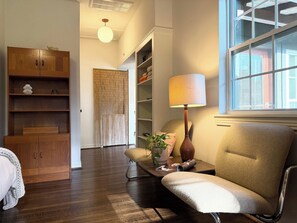 A room with a wooden cabinet, a chair, a lamp, a plant, and a window with blinds. - the escape: king bedroom w/pool, hot tub access (Houston)