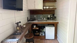 A compact kitchen with a flat-screen TV, wooden cabinets, a coffee machine, and a small refrigerator.