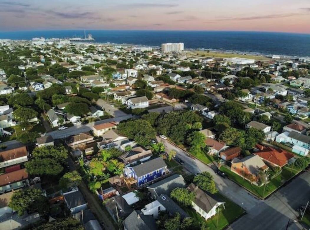 Luftaufnahme eines Wohngebiets mit Häusern, Straßen und einem Blick auf das Meer in der Ferne.