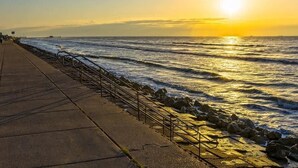 A coastal walkway with a concrete path, metal railings, and a rocky shoreline.