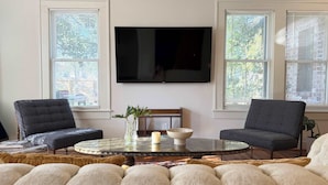 A living room with a round glass coffee table, two armchairs, a sofa, and a flat-screen TV mounted on the wall. - retro elegance - 3 king bedrooms w/pool & hot tub (Houston)