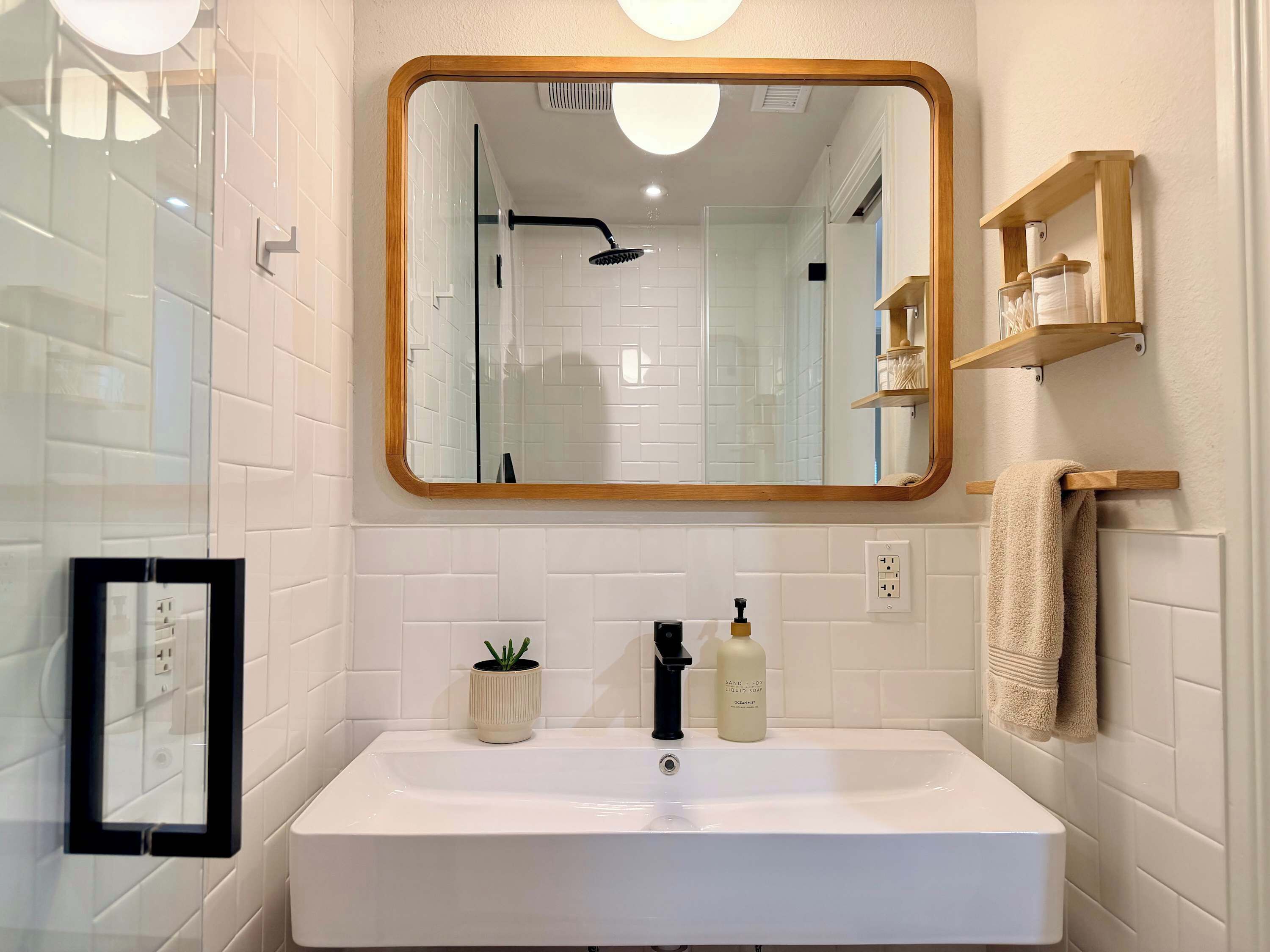 A bathroom with a white sink, a mirror with a wooden frame, a shower, and a towel rack.