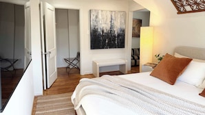 A bedroom with a large bed, a bench, a painting, and a door leading to another room. - retro elegance - 3 king bedrooms w/pool & hot tub (Houston)