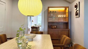 A dining area with a wooden table, chairs, a hanging light fixture, and a glass cabinet with shelves. - retro elegance - 3 king bedrooms w/pool & hot tub (Houston)