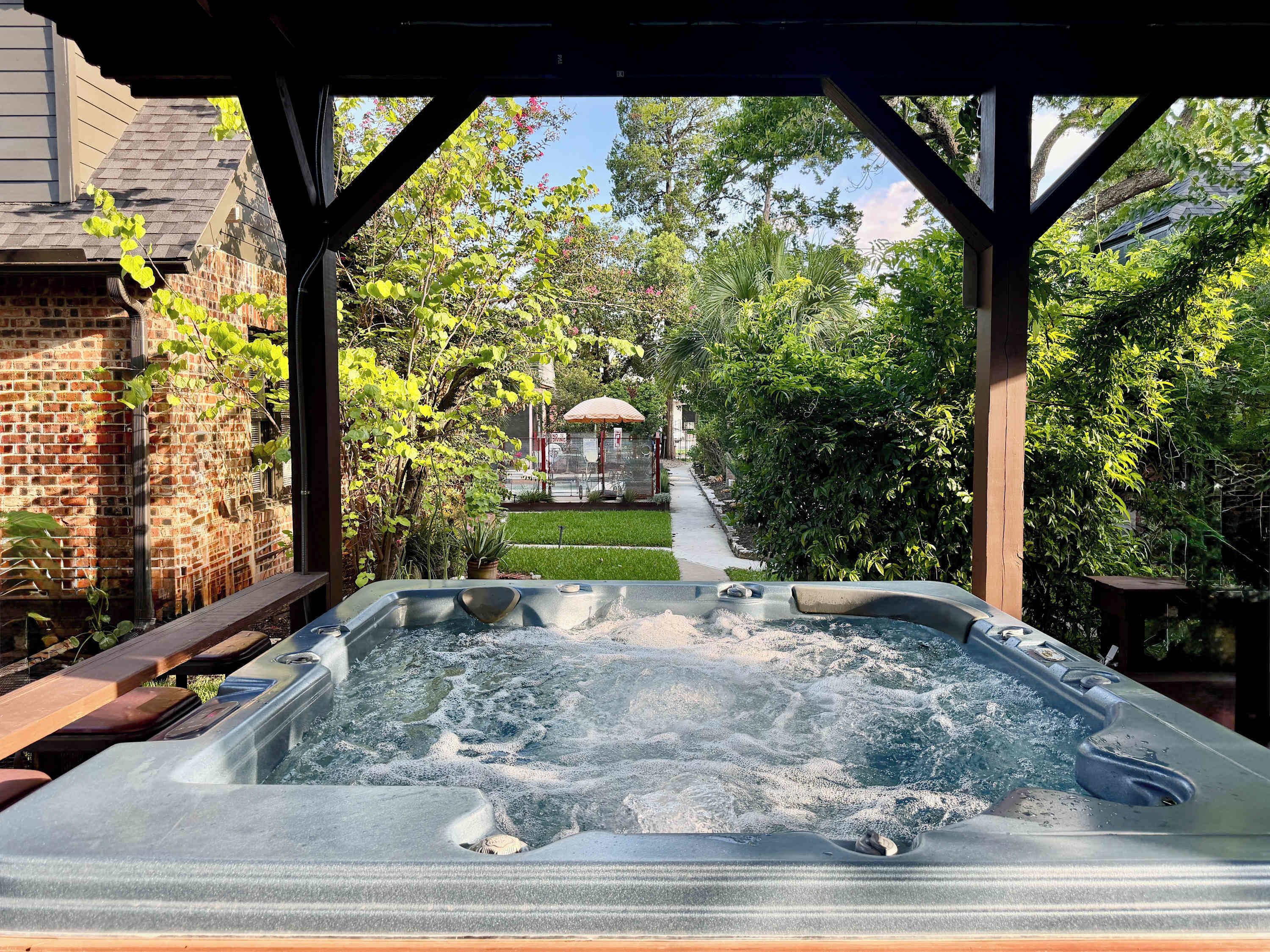 A hot tub in a covered outdoor area with a brick wall and greenery in the background.