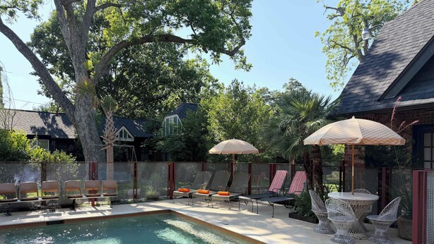 A swimming pool with lounge chairs and umbrellas, surrounded by trees and a fence. - retro elegance - 3 king bedrooms w/pool & hot tub (Houston)