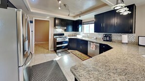 A modern kitchen with dark cabinets, a stainless steel refrigerator, a gas stove, and a granite countertop. - Zia Peak (Ruidoso)