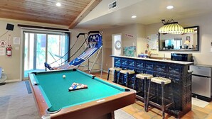 A pool table with a pool cue and balls, a bar area with stools, and a kitchen with a refrigerator. - Zia Peak (Ruidoso)