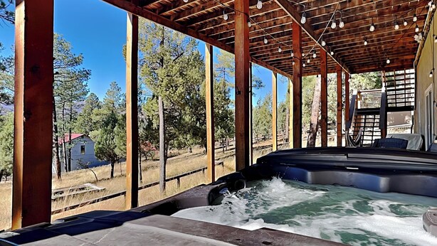 A hot tub under a wooden pergola with a view of trees and a small building. - Zia Peak (Ruidoso)