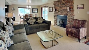 A living room with a stone fireplace, a sofa, a patterned armchair, and a glass coffee table. - Zia Peak (Ruidoso)