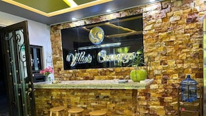 Una zona de bar con pared de piedra, un letrero de neón, taburetes y un dispensador de agua.