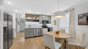 Una cocina moderna con armarios grises, un refrigerador de acero inoxidable y una zona de comedor con una mesa redonda y cuatro sillas.