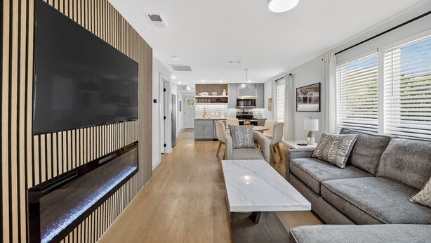 Una sala moderna con un televisor de pantalla plana, un sofá, una mesa de centro y una cocina al fondo.
