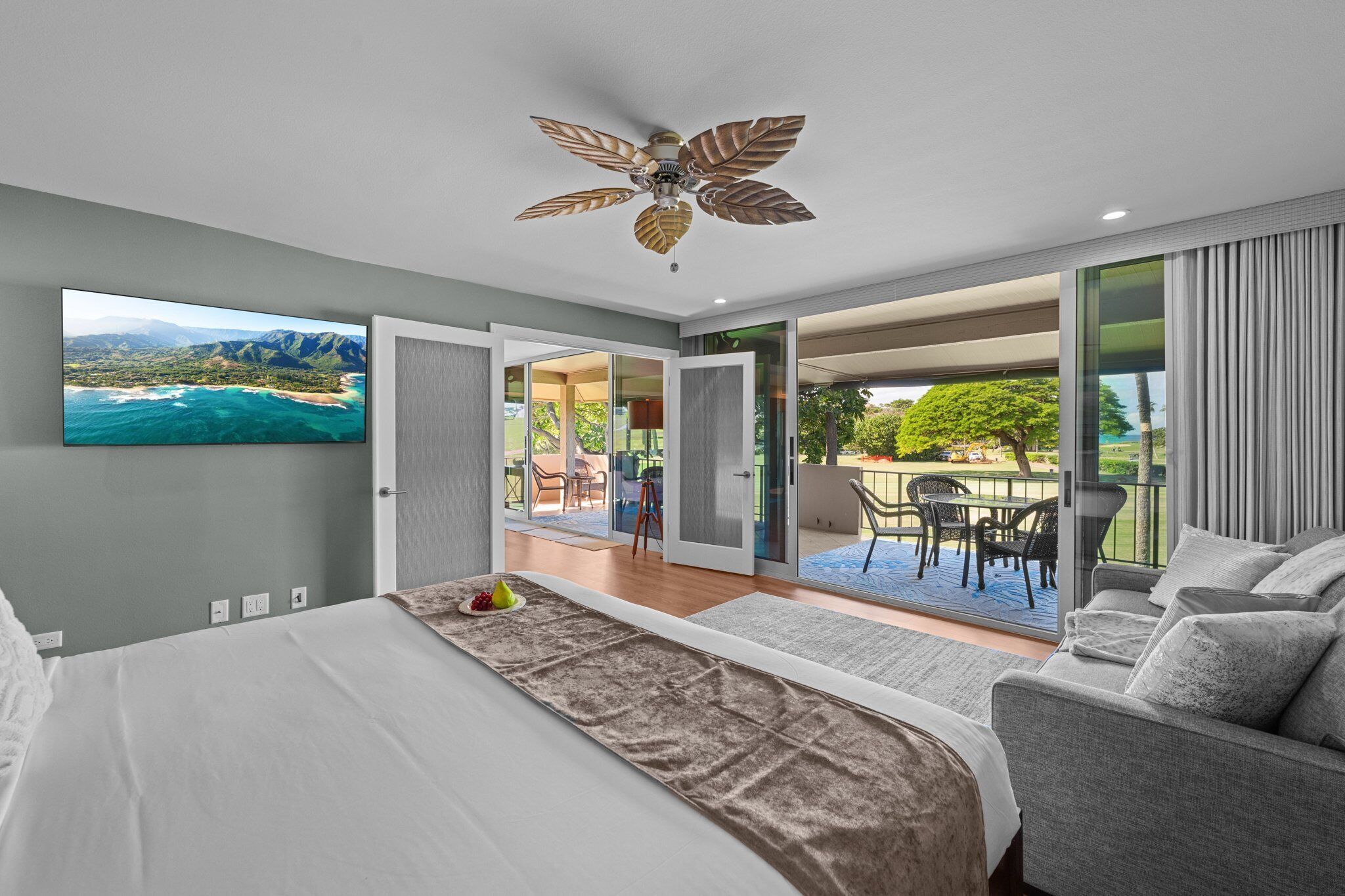 A bedroom with a bed, a ceiling fan, a TV, and a balcony with outdoor furniture.