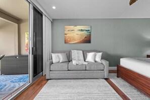 A modern bedroom with a grey sofa, a wooden bed, and a large beach painting on the wall. - West Maui Oasis: Ocean and Golf Views (Kaanapali)