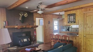 A cozy cabin interior with a fireplace, wooden walls, a dining area, and a kitchen. - Pinetop Vista - The Wildlife Cabin (Pinetop)