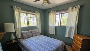 A bedroom with a bed, two windows with curtains, a dresser, and a lamp. - Pinetop Vista - The Wildlife Cabin (Pinetop)