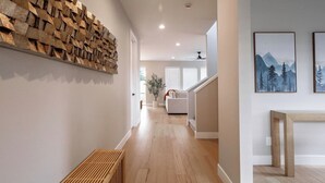 A hallway with a wooden bench, a wall-mounted wooden art piece, and a staircase leading to a living area with a sofa. - Evergreen Dream-massage chair, EV, 5tvs,3 king bed (Vancouver)