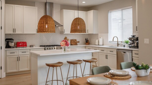 A modern kitchen with white cabinetry, a central island with stools, and pendant lighting. - Evergreen Dream-massage chair, EV, 5tvs,3 king bed (Vancouver)