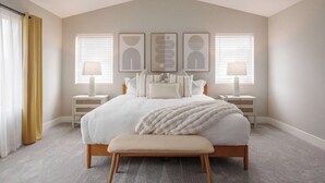 A bedroom with a large bed, two bedside tables, a bench, and three wall-mounted artworks. - Evergreen Dream-massage chair, EV, 5tvs,3 king bed (Vancouver)