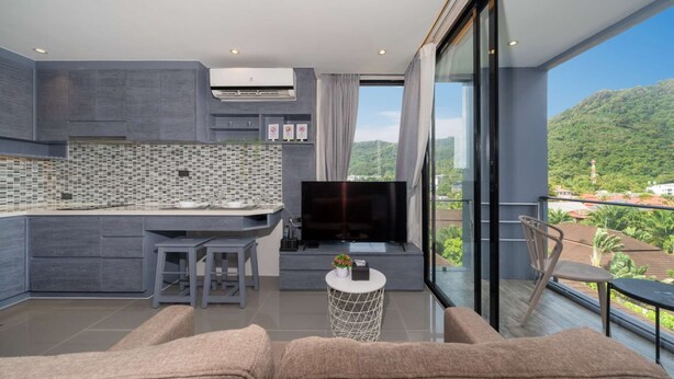 Una cocina moderna con una televisión de pantalla plana, un comedor con taburetes y un balcón con vistas a las colinas.