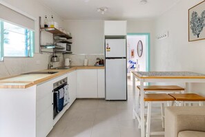 A compact kitchen with white cabinetry, a built-in oven, a refrigerator, and a wooden dining table with benches. - Self contained studio near the boat club with deck (Yorkeys Knob)