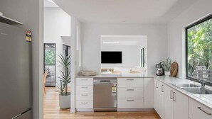 Een moderne keuken met witte kasten, een inbouwvaatwasser en een groot raam met uitzicht op groen.